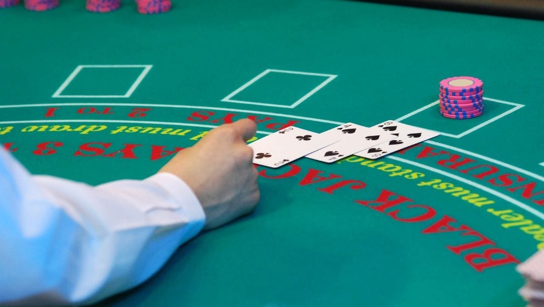 A dealer placing a card on the blackjack table, with other cards and casino chips arranged on the table.