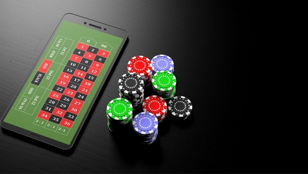Smartphone resting on a table, displaying an open roulette game on its screen, with poker chips stacked across the table.