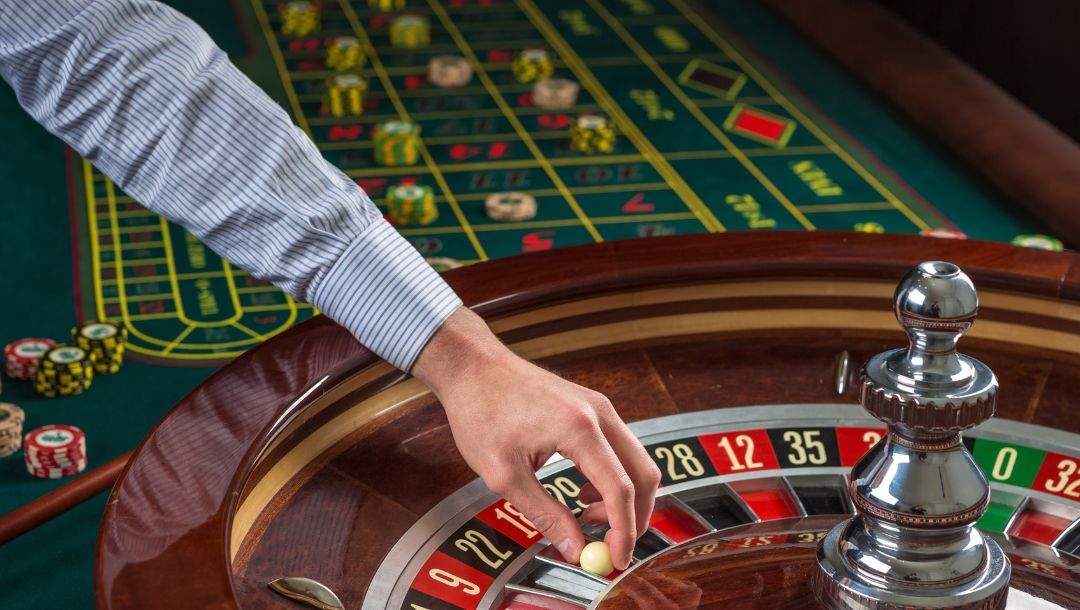 Croupier hand placing a ball on a roulette wheel.