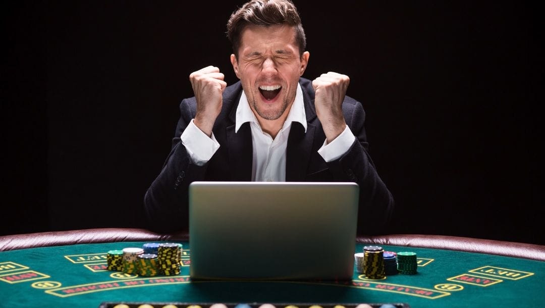 A person celebrating a victory in front of a laptop, while seated at a poker table.