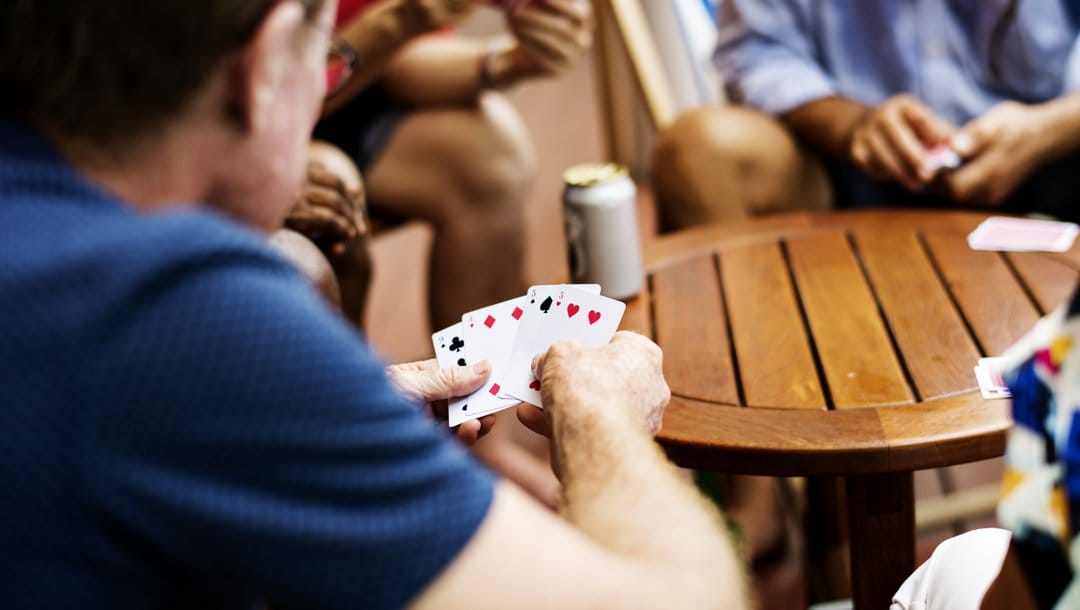 A group of friends playing cards around a wooden table.