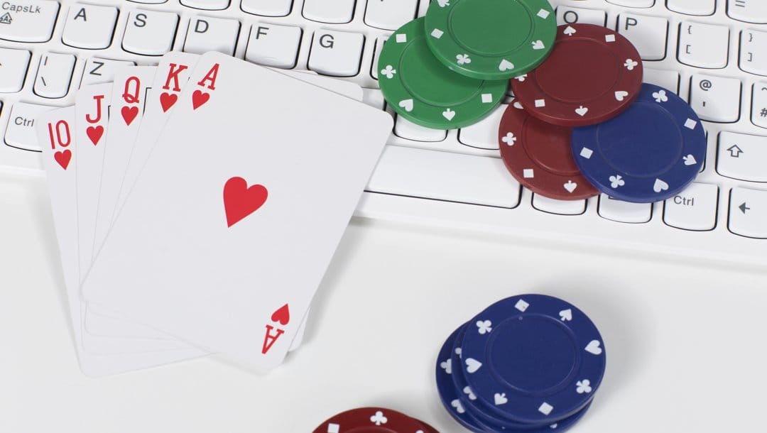 A royal flush sitting on a keyboard next to scattered poker chips.