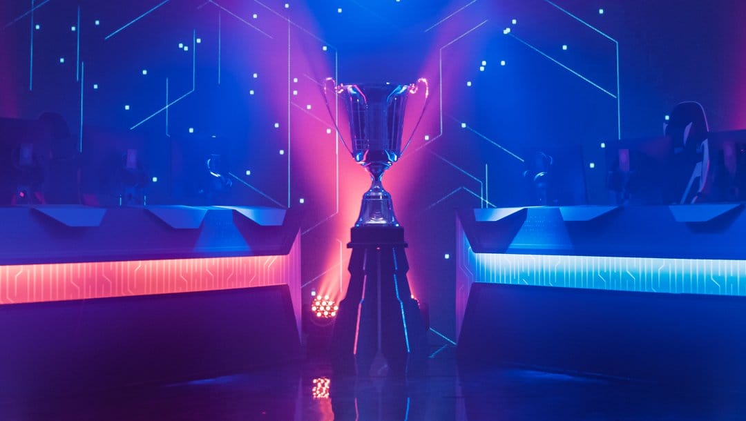 A trophy between two sets of computers on a stage with neon lighting.