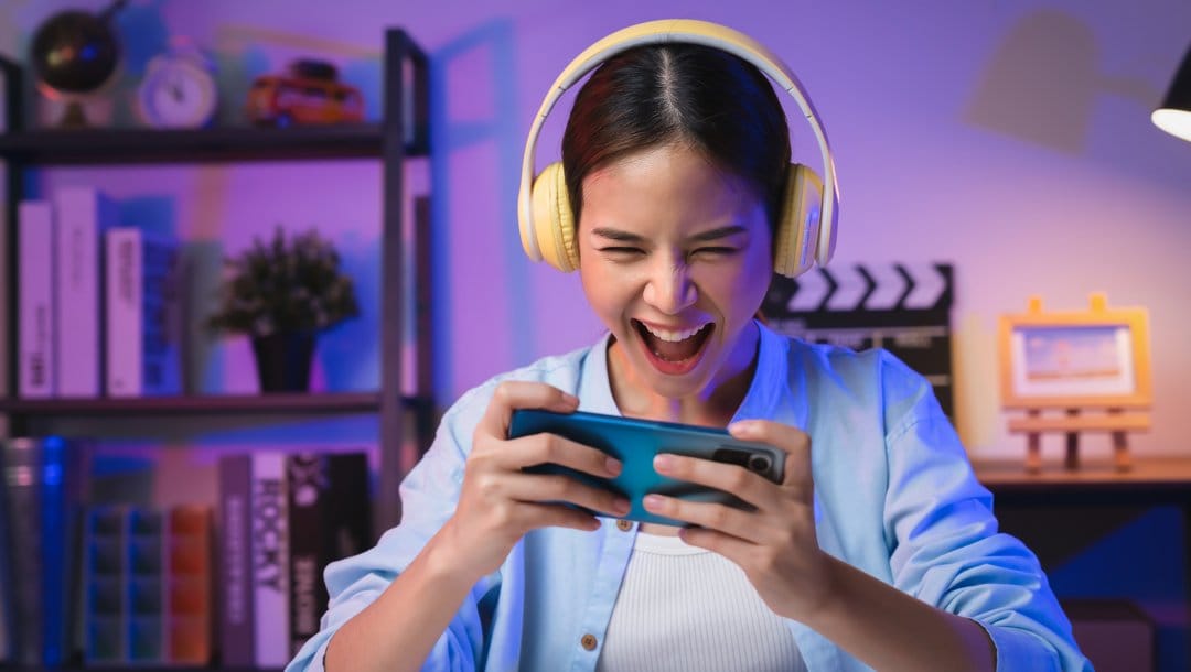 A person wearing headphones playing a game on their mobile phone.