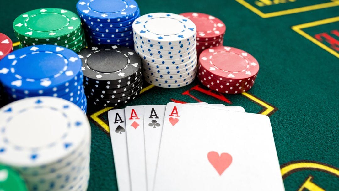 Four aces sitting on a casino table surrounded by stacks of poker chips.
