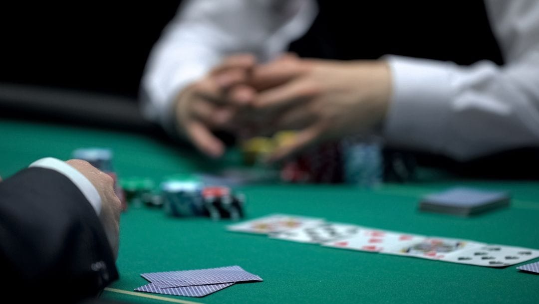 a person sitting opposite a dealer at a poker table with playing cards and poker chips on it during a poker game