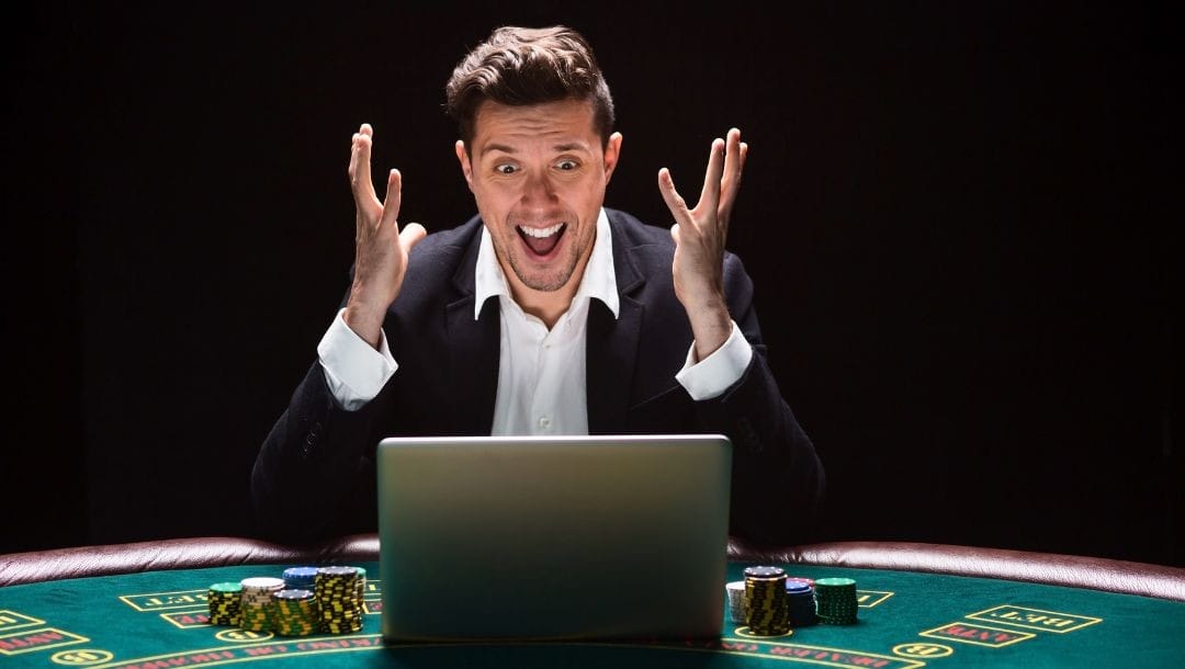 a man is cheering while sitting at a poker table with a laptop open in front of him