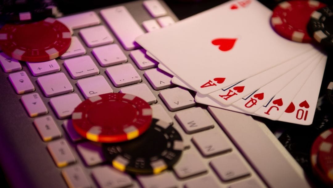 a royal flush of hearts playing cards and red and black poker chips on a computer keyboard