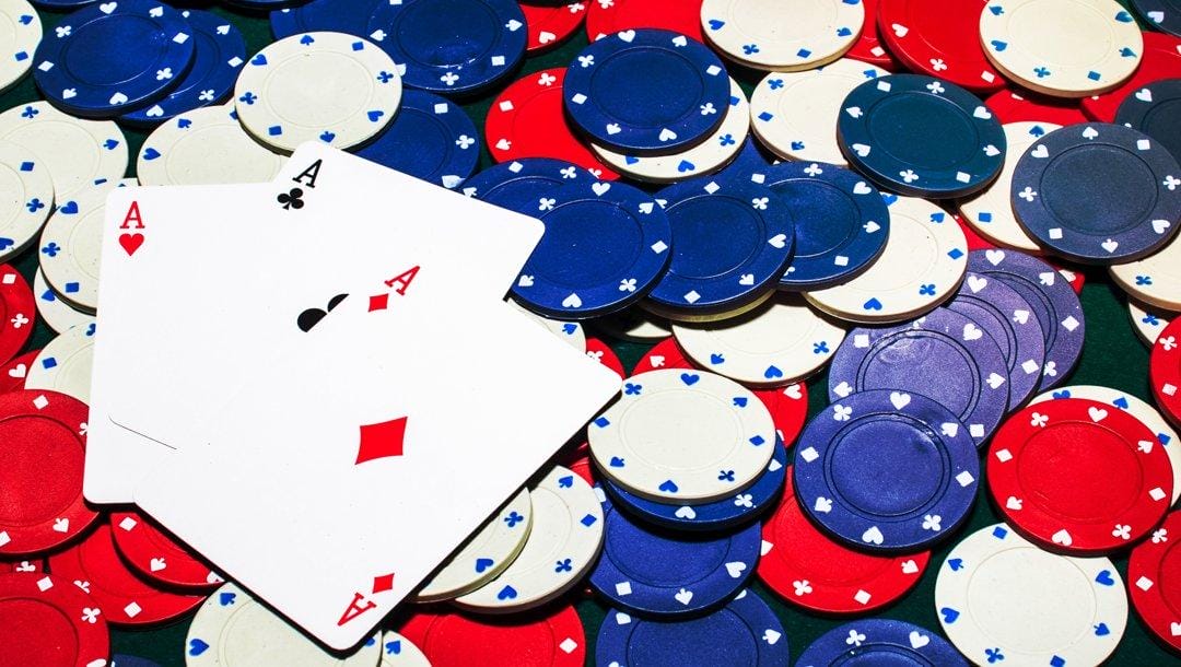Three aces lying on scattered blue, red, and white poker chips.
