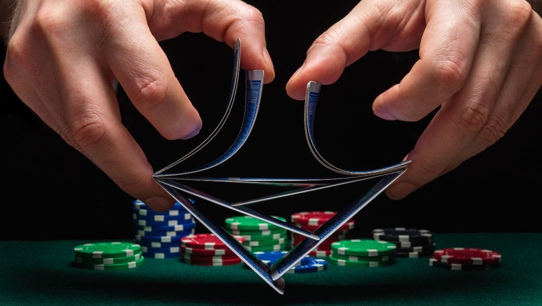 Close up of a person’s hands shuffling cards in the air above a green felt poker table with poker chips stacked on the in the background.