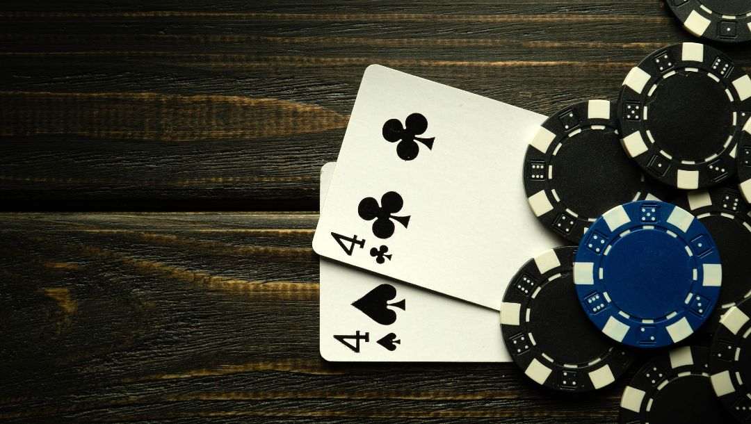 a pocket pair of fours underneath black and blue poker chips on a wooden surface
