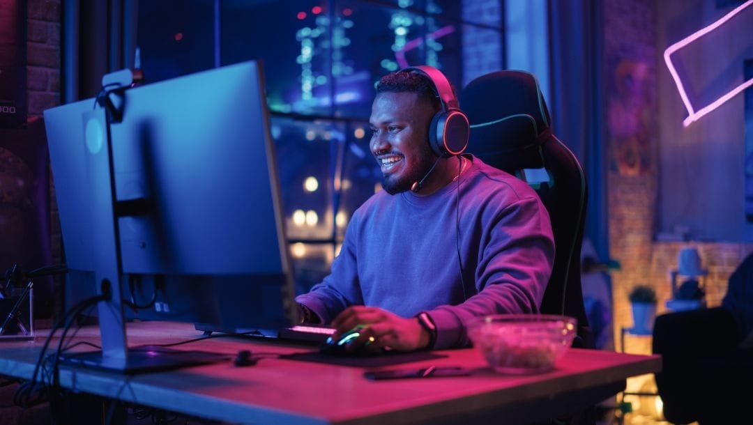 a man gaming at a desk on a PC in a room with ambient lighting