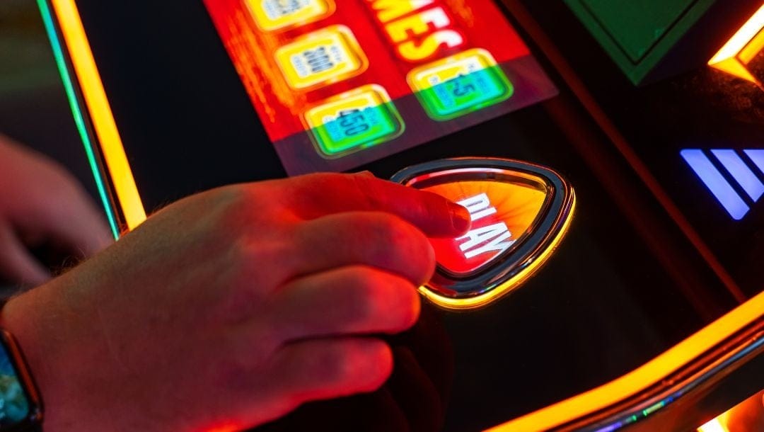 close up of a person’s hand as their index finger presses the “play” button on a slot machine
