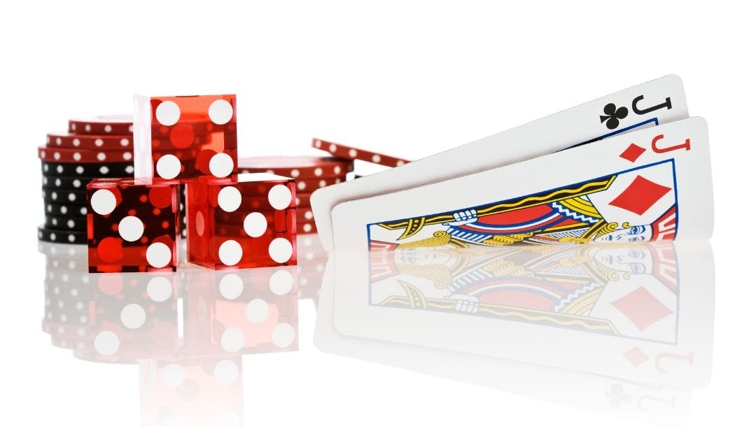 An image showing pocket jacks, three red dice, and red poker chips on a reflective white table.