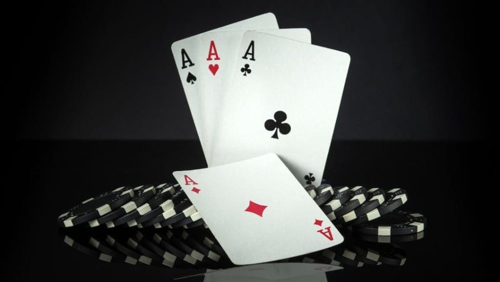 Quad Aces balancing upright on top of black poker chips, on a reflective black surface with a black background.