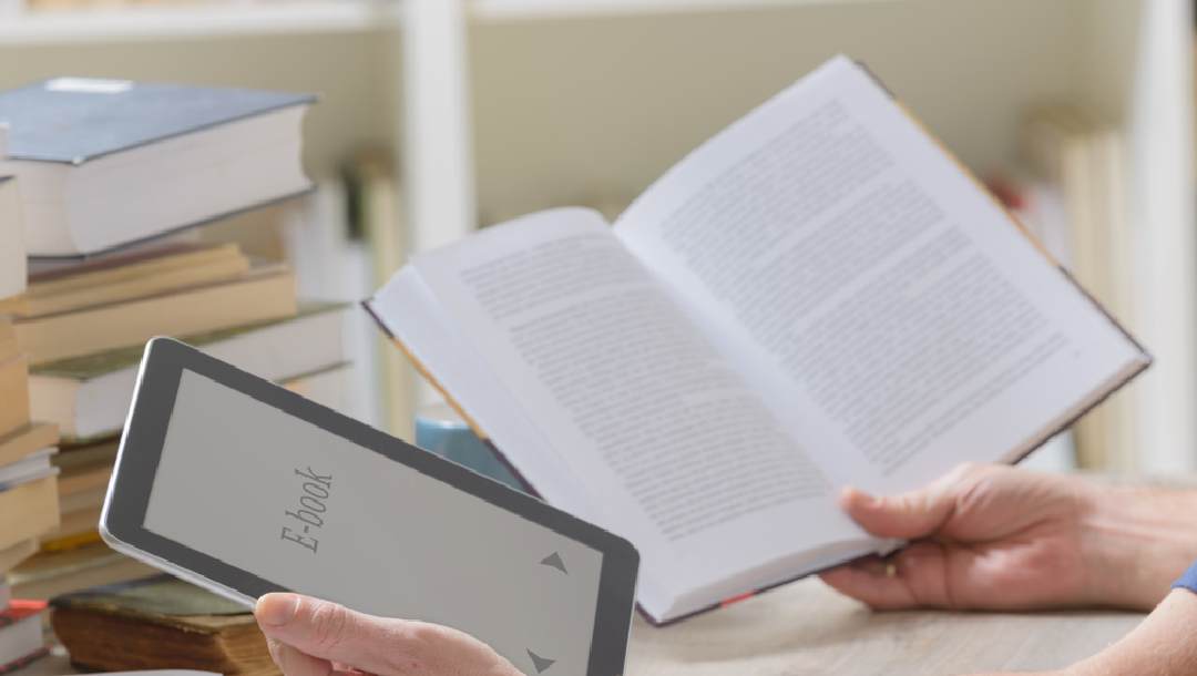 A person holding an e-book and a physical book next to each other.