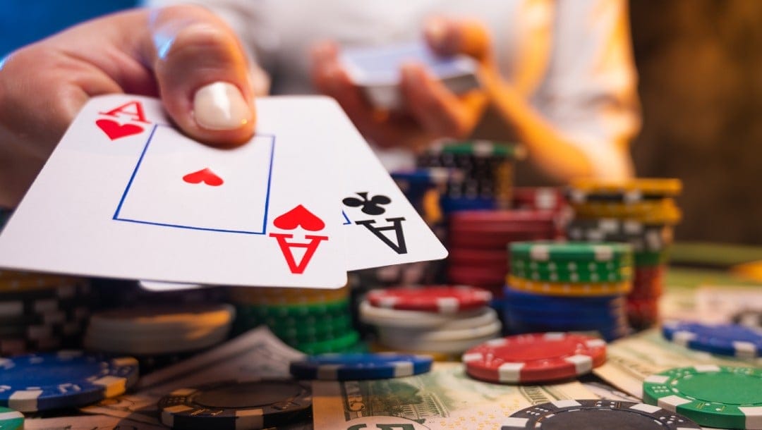 Poker playing cards in hand with poker chips and money on the table.