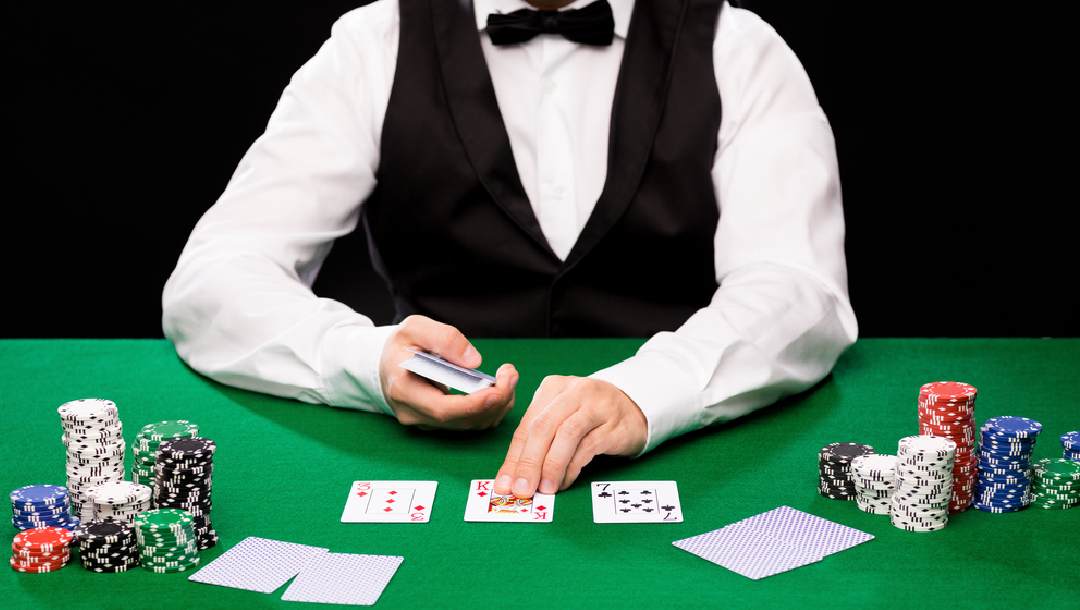 A poker dealer putting cards down on a green felt table.
