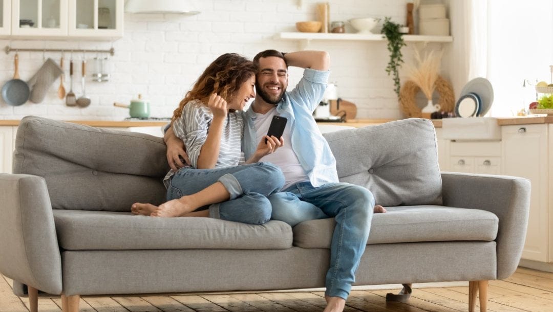 A couple sitting on a couch with a smartphone.