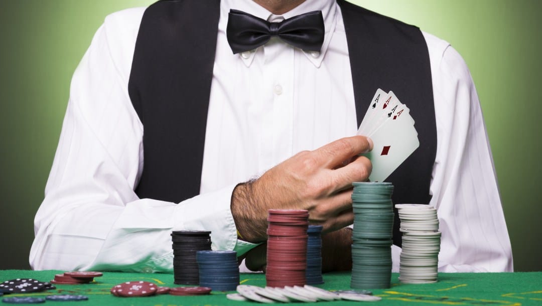 A poker dealer holding poker cards in front of a poker table with chips.