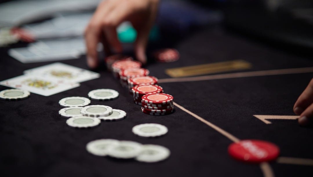 A hand picking up red poker chips on a black poker table.