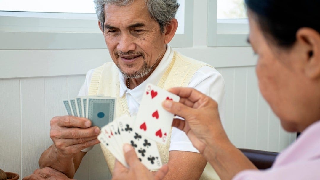 Two people holding playing cards sit across from each other