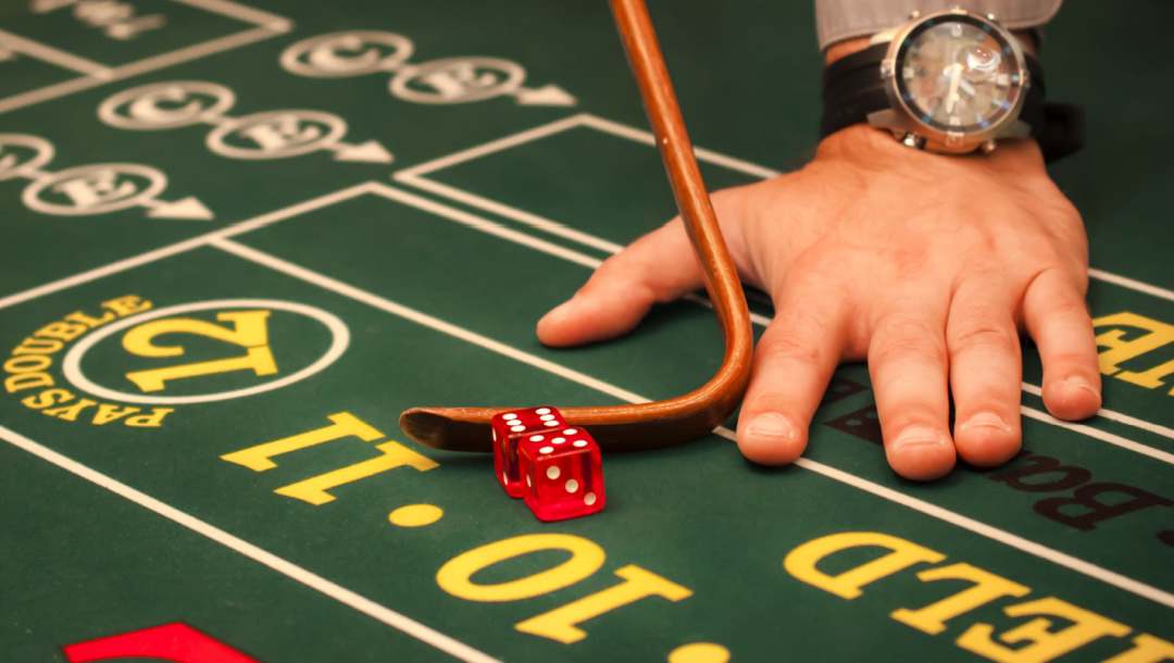 A close up of a craps table and a dealer’s hand with dice and a craps mop