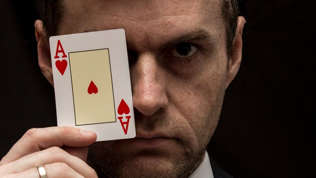 A man holds an ace of hearts in front of his left eye.
