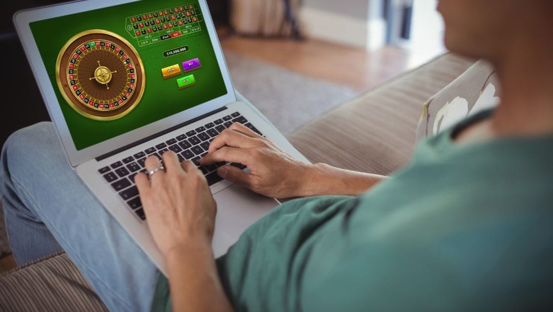 A person sitting on a couch, playing a game of online roulette, on a laptop.