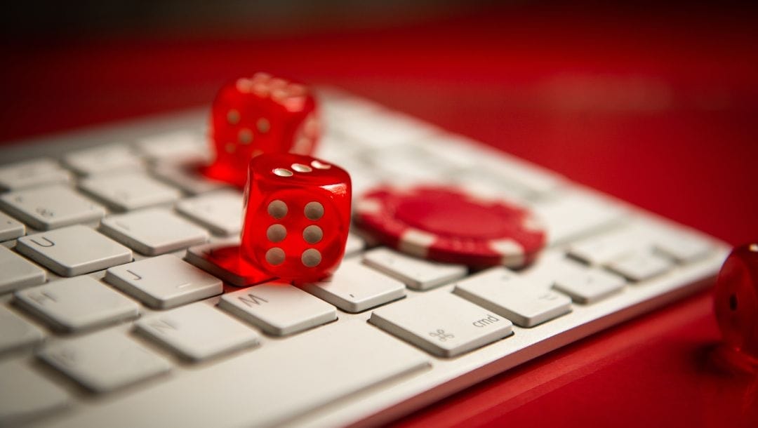 Two red dice, and a red casino chip resting on a white computer keyboard.