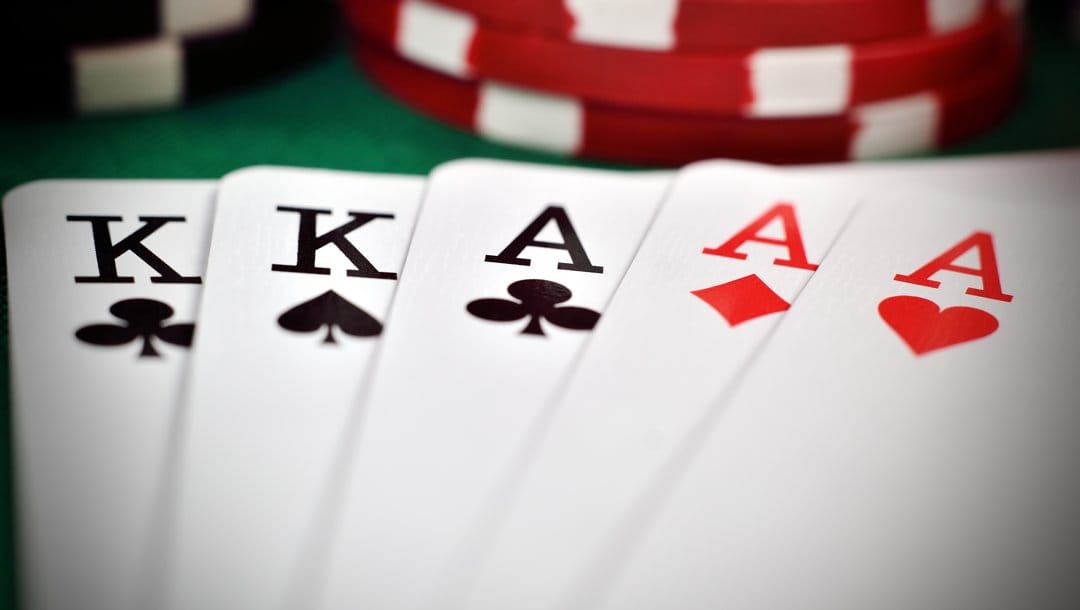 A close-up of a full house poker hand sitting on a poker table. The hand consists of two kings and three aces. There are stacks of poker chips in the background.