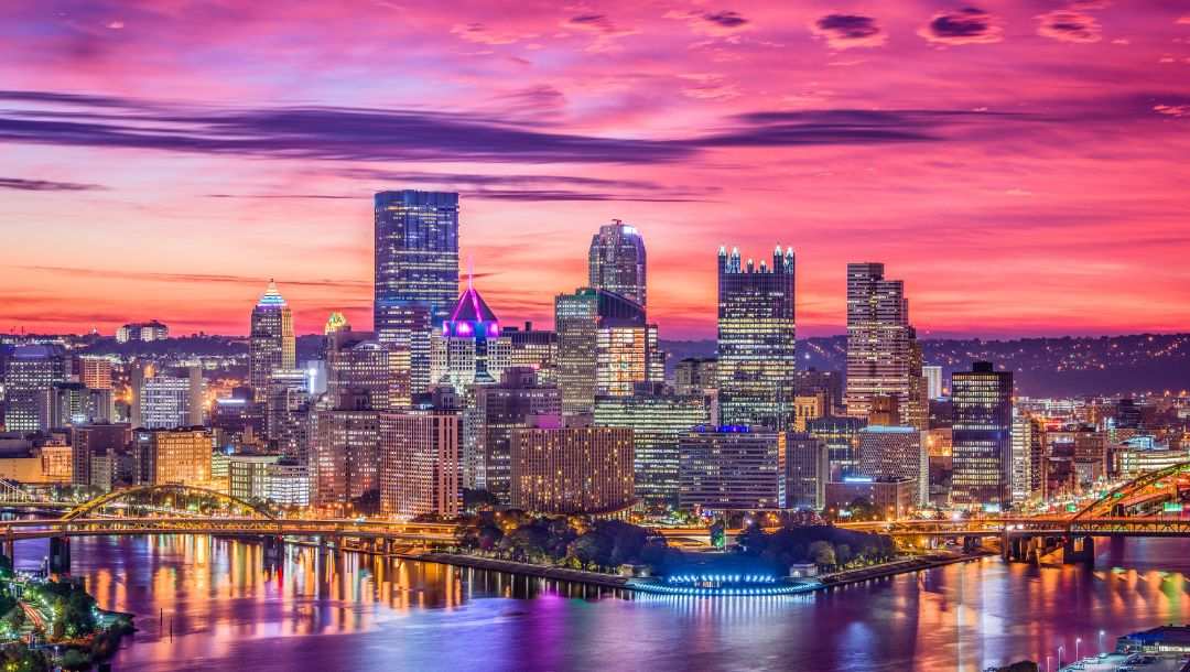 A panoramic view of a skyline in Pittsburgh, Pennsylvania with a sunset in the background.