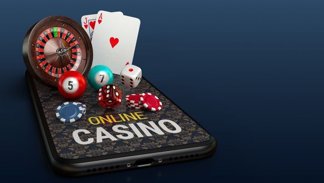 A smartphone on an online casino website with small poker chips, dice, pool balls, playing cards, and a roulette wheel on top of it.