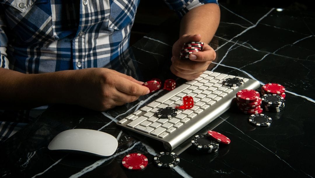 A man holds poker chips over a Bluetooth keyboard that also has poker chips on it, and a Bluetooth mouse, all on a marble countertop.