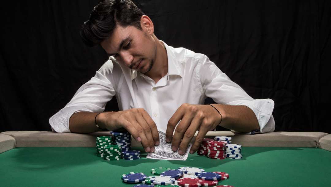 A poker player taking a look at his hand with his chips in font of him