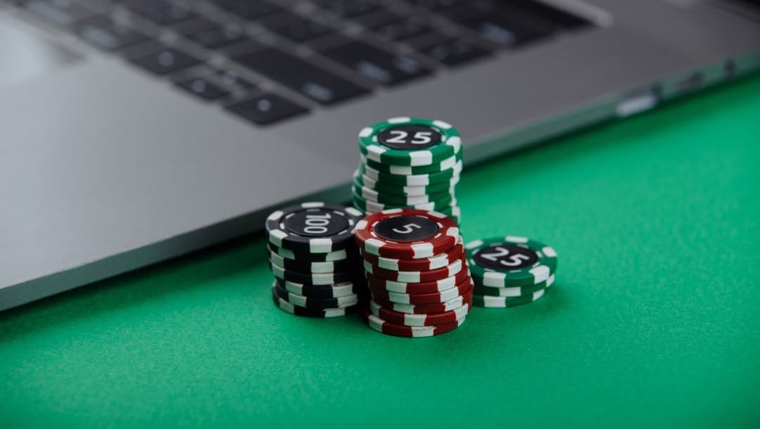 Casino chips and a laptop on a green felt table.