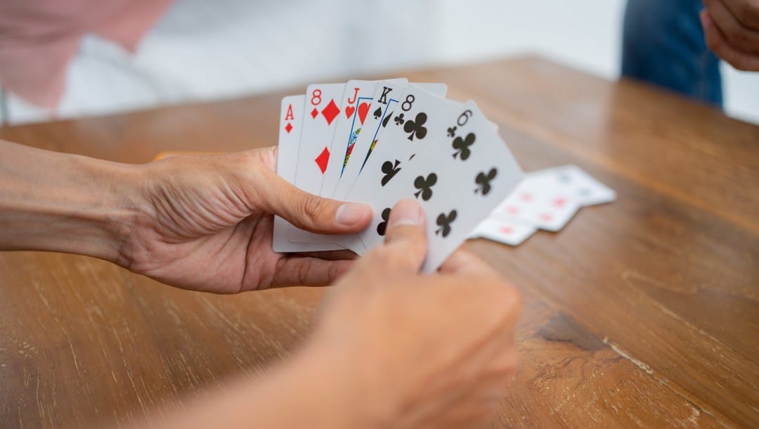 Hands holding playing cards on a brown table.