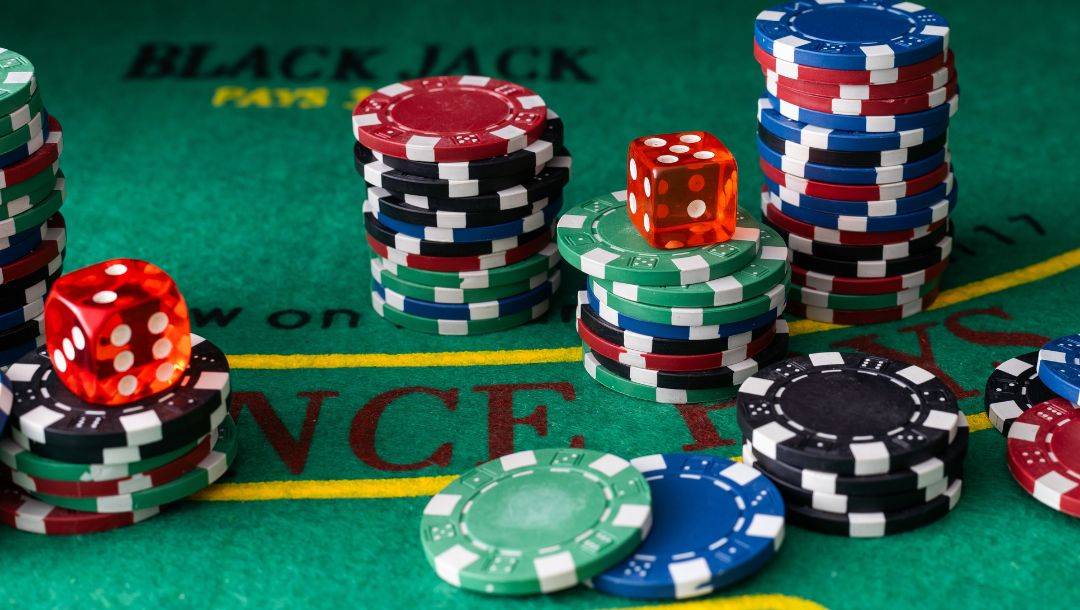 Stacks of black, red, blue, and green poker chips, and a red dice, arranged on a poker table.