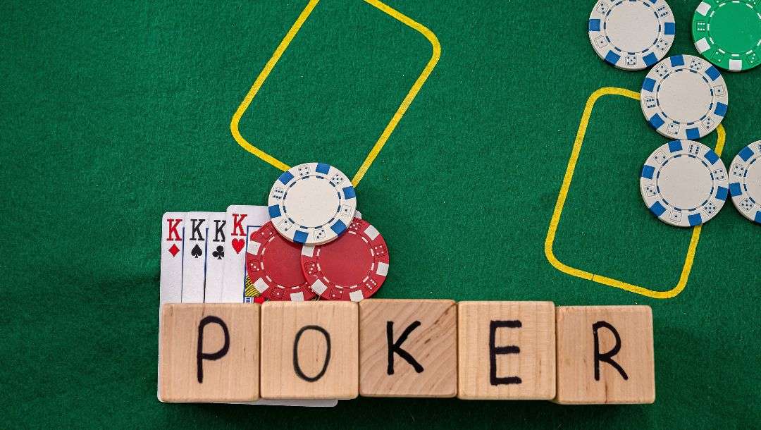 Four King playing cards, poker chips, and five wooden blocks spelling out the word “poker” on a green felt table.