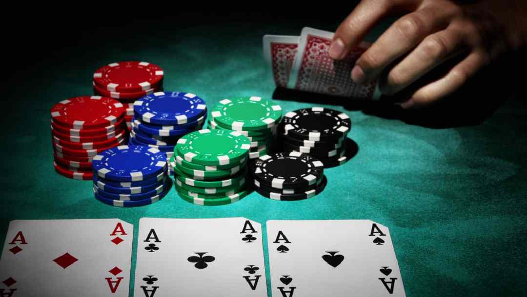 Three aces and chips on a poker table with a player’s hand in the background