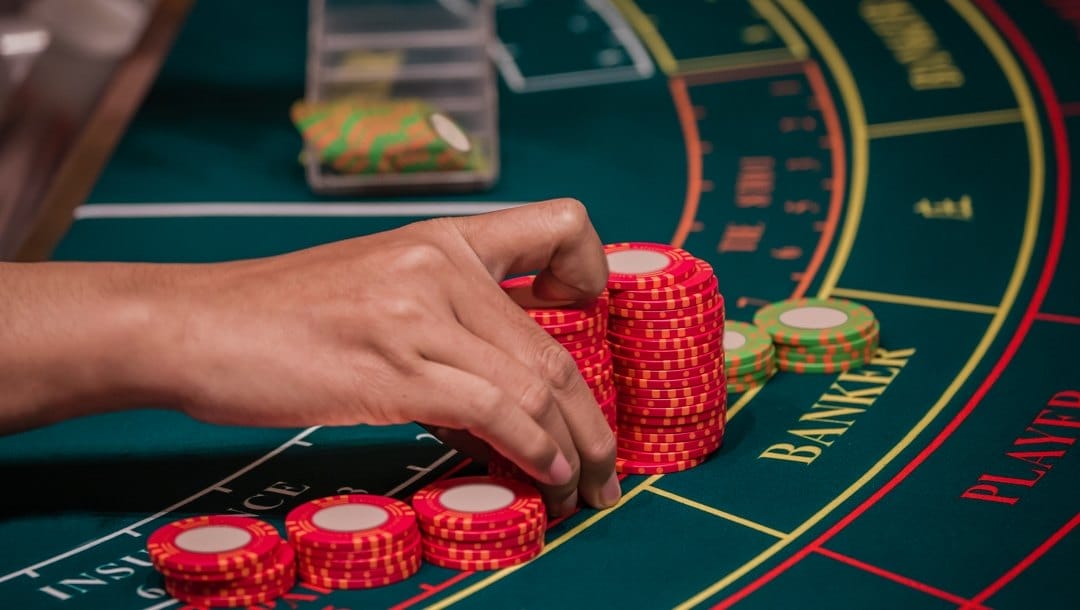 A hand of dealer organizing red and green poker chips on baccarat gaming table