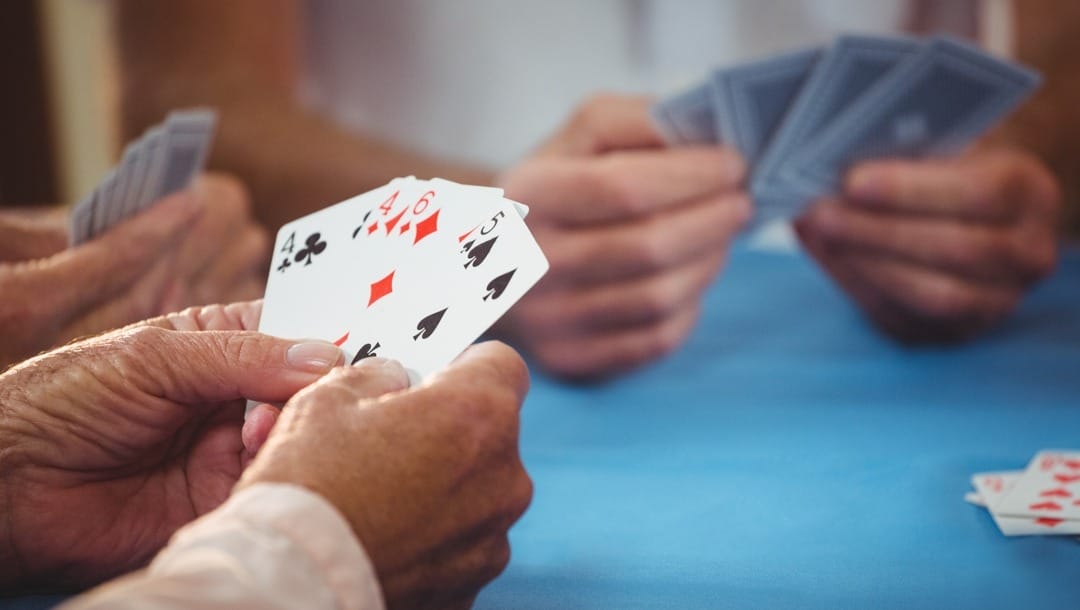Three pairs of hands hold playing cards on a blue table