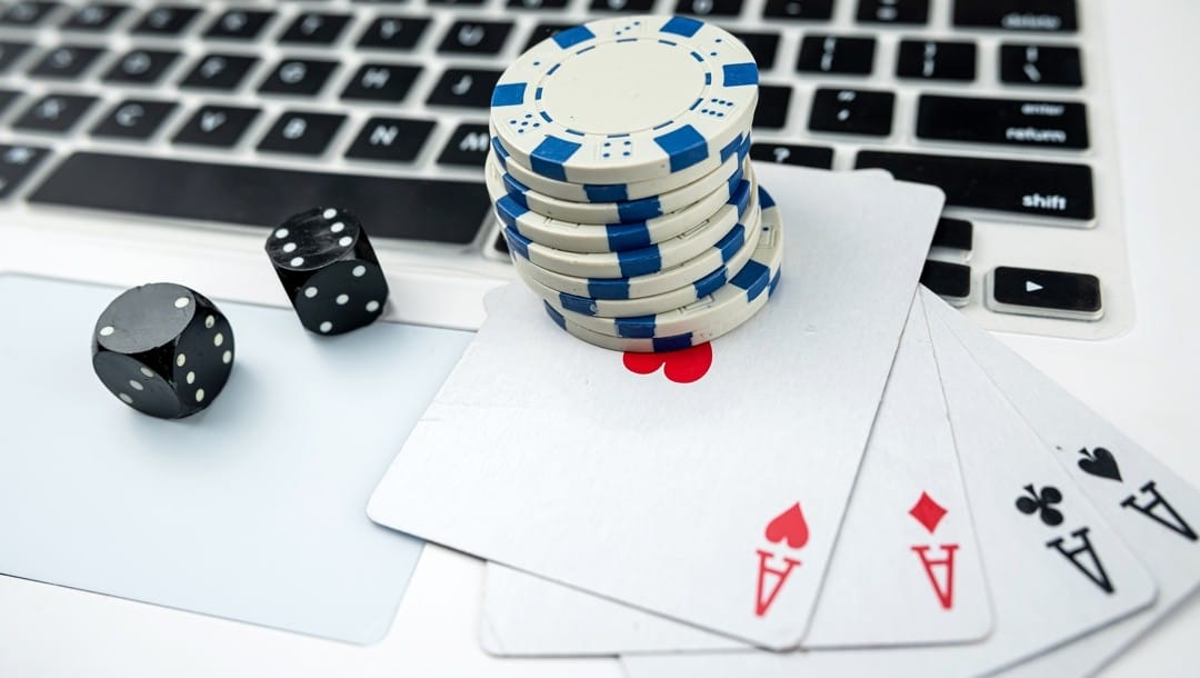 Online poker on laptop with two black dice, playing cards, and casino chips