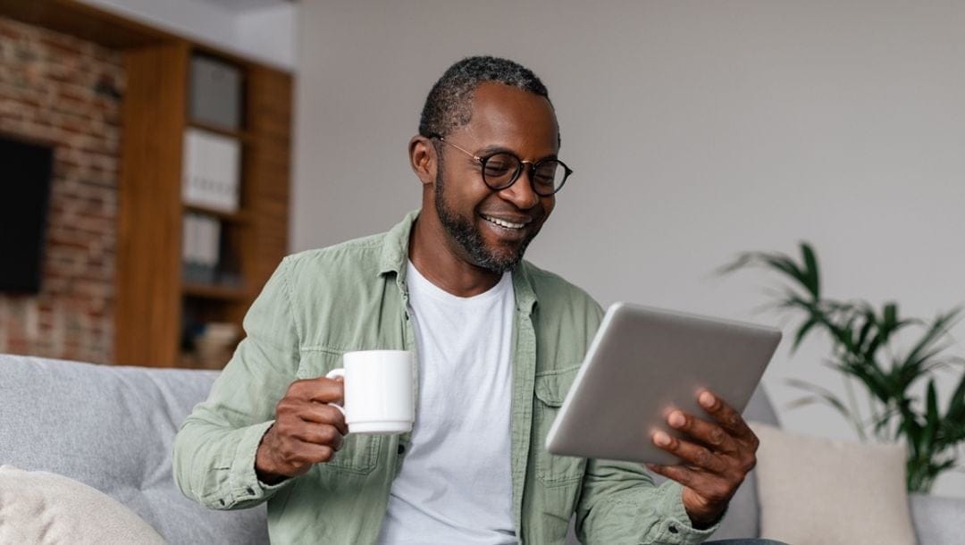 A man looking at his tablet screen with a cup of coffee in one hand.