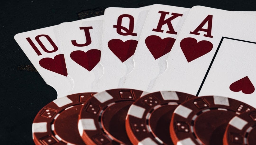 A Royal Flush with five red and white poker chips on top of the cards.