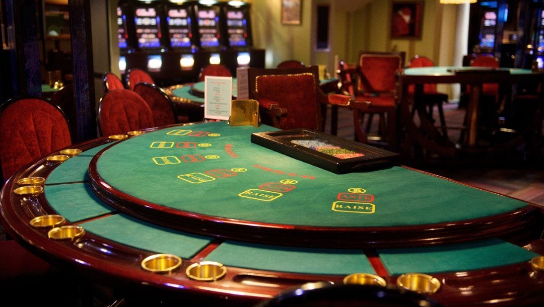 An empty casino game table with casino chips in a casino. Slot machines and other casino tables are visible in the background.