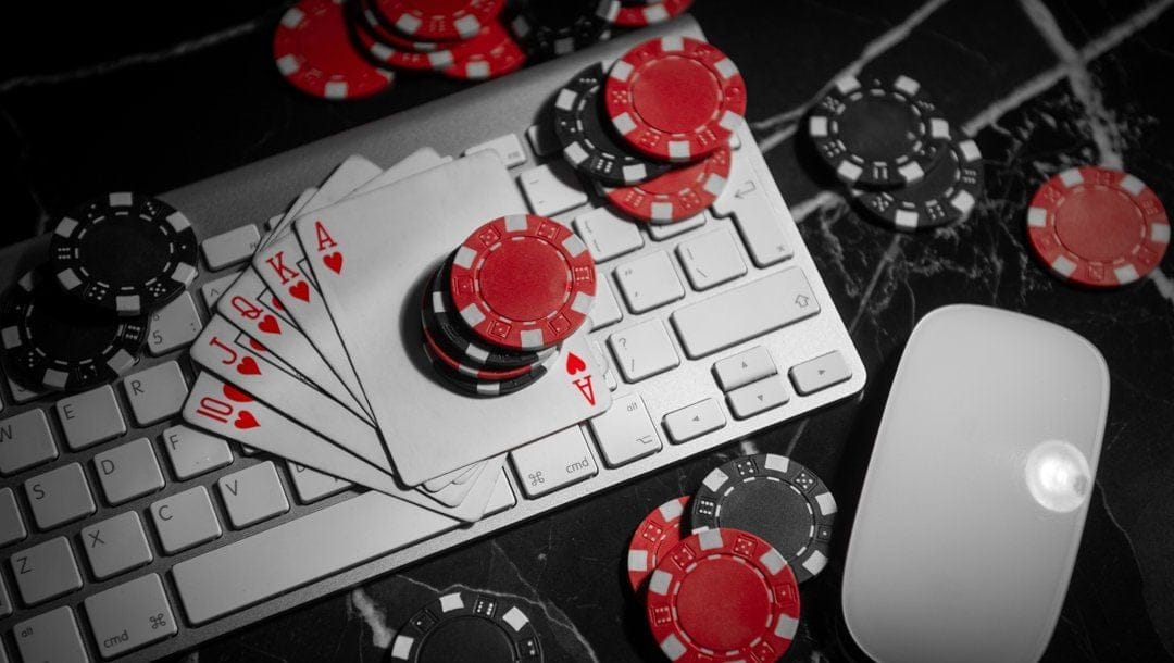A royal flush on a white and gray keyboard. Stacks of black and red poker chips surround it. A white mouse is next to the keyboard.