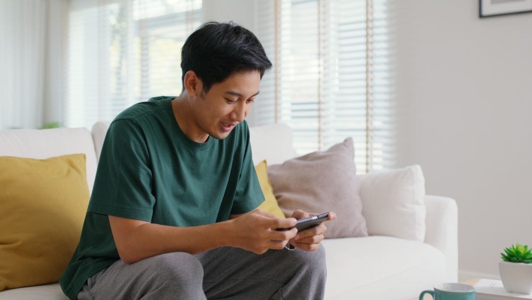 Man playing on his phone while seated on a couch.