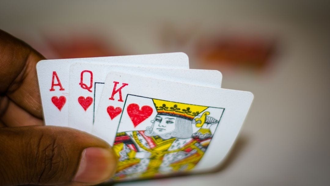 A hand discreetly revealing an ace, queen and king of hearts.