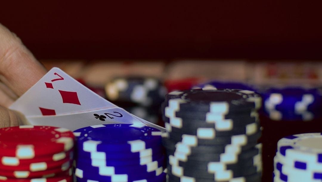 Organized stacks of poker chips by color, hand revealing 7 of diamonds and 2 of clubs in the background.